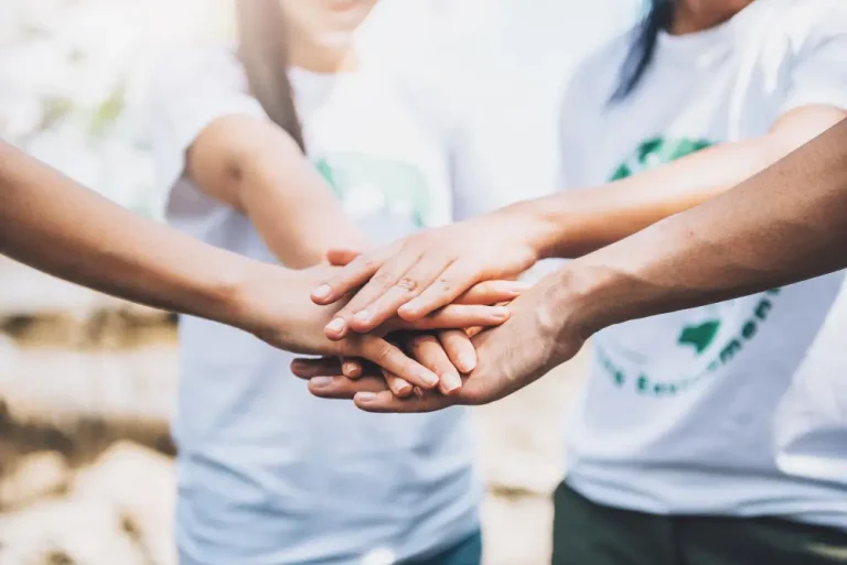 About Us 2 Hands of three people wearing white t-shirts joined together in solidarity.